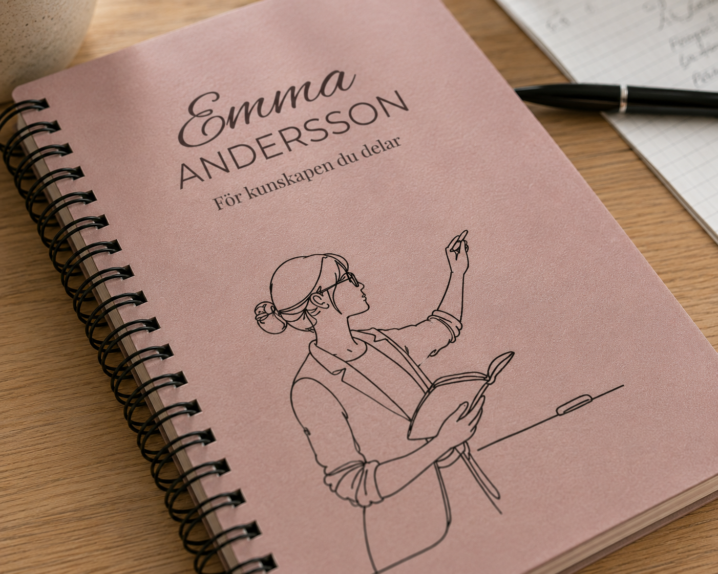 Närbild på personlig anteckningsbok med namnet Emma Andersson och lärarmotiv på rosa omslag